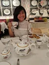 Alison holding a tea cup sitting indoors with a teas set on her table.