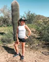 Amy Jay stands in front of a cactus looking in running attire and a baseball hat, looking to the right of the frame.