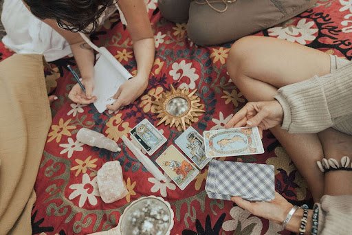 People seated in a circle on a red print carpet around Tarot cards and crystals.