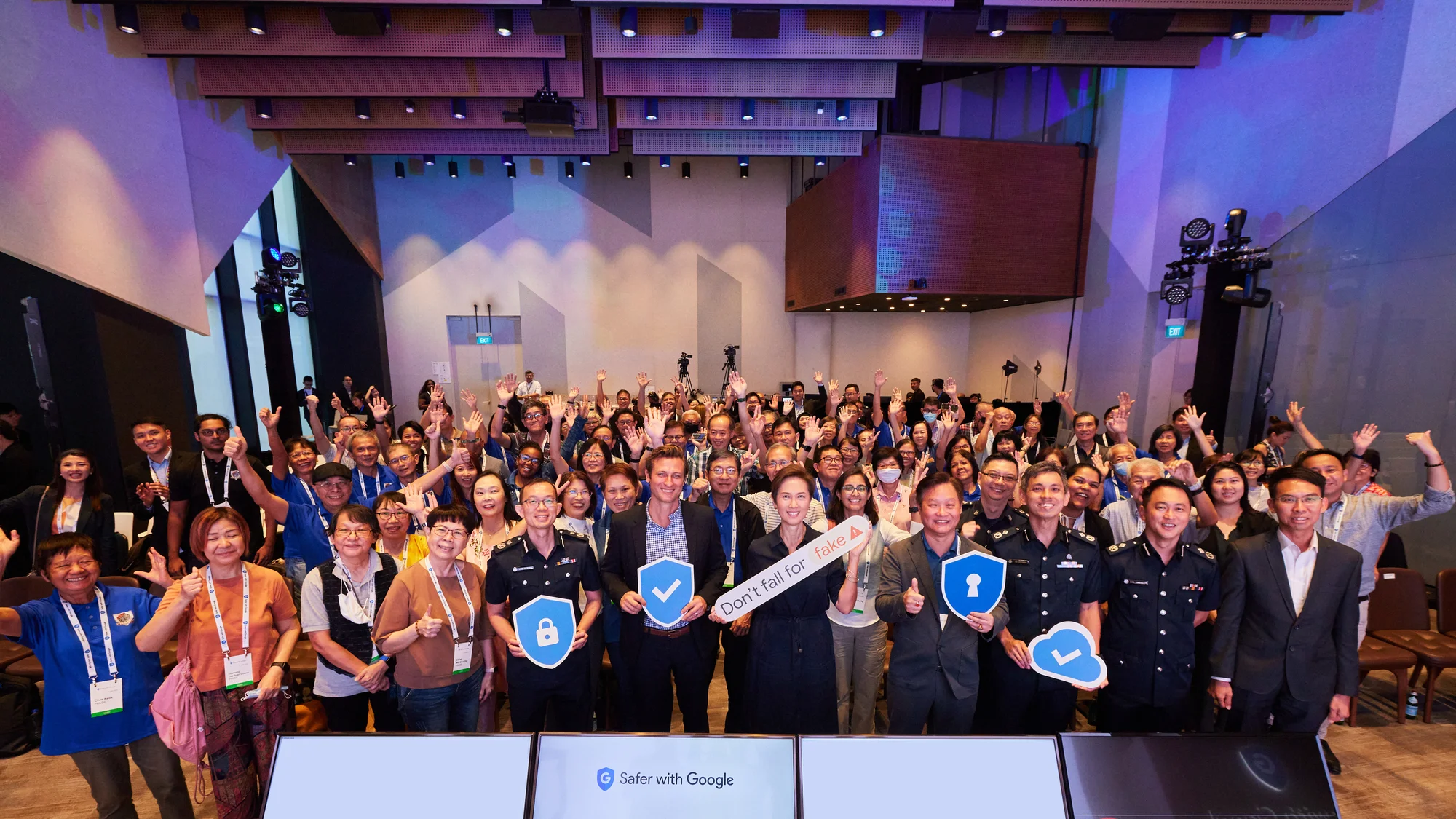 A large crowd of people indoors looking at the screen, with a small screen in front of them that reads "Safer with Google"