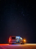A photo captured using Night Sight with Astrophotography shows a brightly lit car at night while also capturing the vivid stars above in the sky.