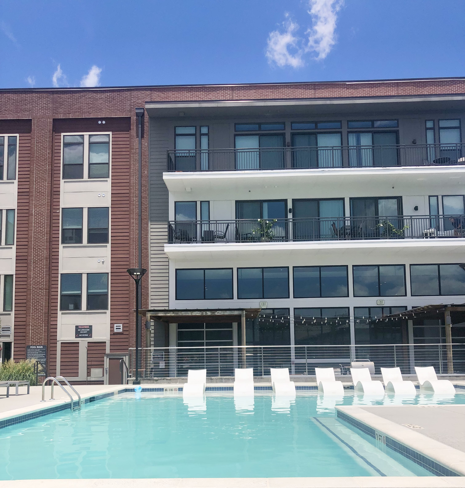 A pool with white lounge chairs underneath a brick apartment building.