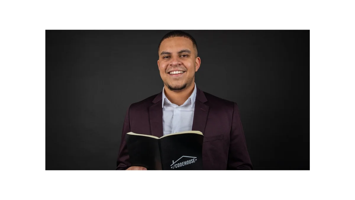 Image showing a man in a suit holding a book that says "CodeHouse" on it. He is looking into the camera and smiling.