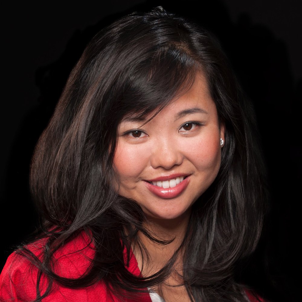 A photo of a woman with long brown hair and a red shirt smiling, with a black background