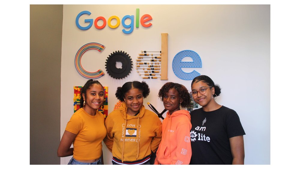 Image shows four young people looking into the camera and smiling and on the wall behind them are the words "Google" and "Code."