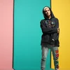 YouTube Creator Daniel El Travieso stands in front of a striped wall wearing jeans and a multicolor Mickey Mouse hoodie