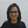 Deeksha, wearing glasses and a black shirt, smiles at the camera.
