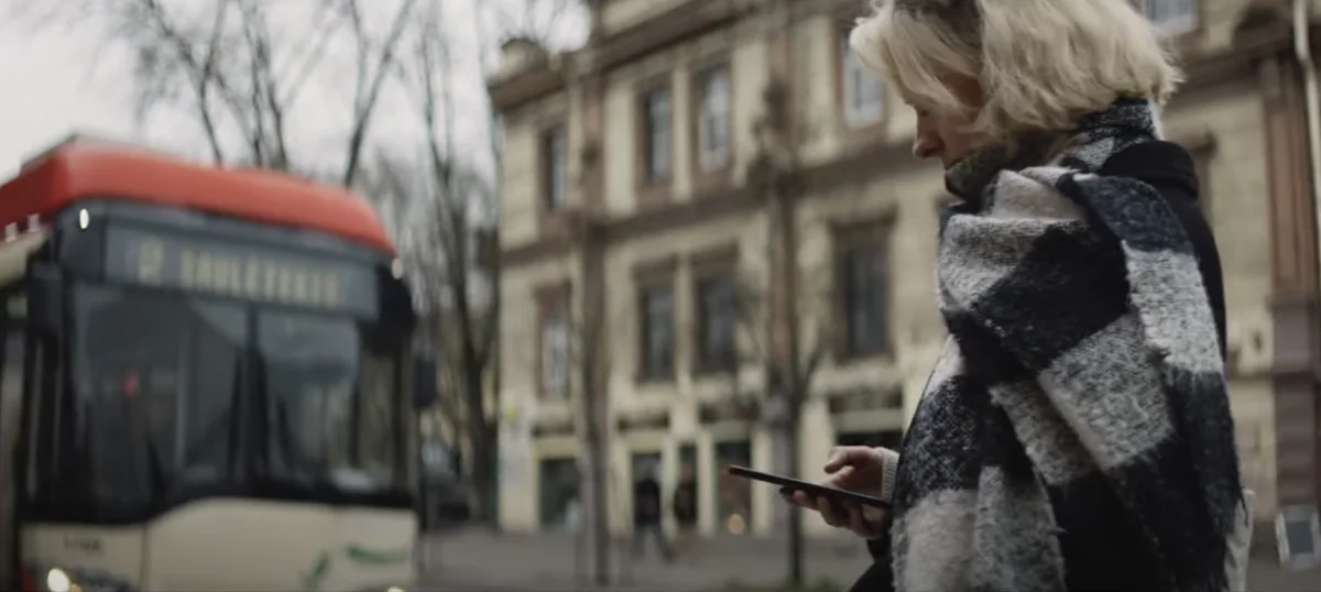 A woman looks at news on her mobile phone as a tram arrives in a European town.