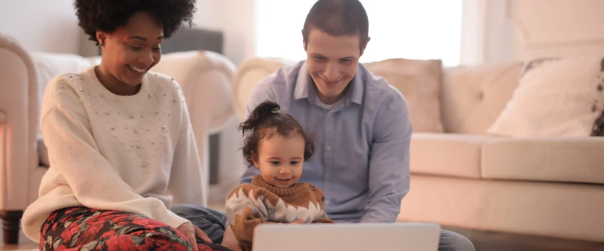 A mother, father and baby look at a laptop screen.