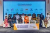 The image captures a group of individuals on stage for the 2023 Hustle Academy SME Fund Recipients event. Two people are seated in the foreground with others standing in a row behind them, all facing the camera with smiles. The backdrop features company logos and the event title, along with the Google Hustle Academy logo.