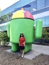 Preeti standing in front of a large Android statue wearing a Noogler hat.