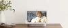 Image showing a Nest Hub Max sitting on a table. On the screen is an older women, looking out, smiling; in a small, picture in picture screen in the corner is a younger woman, smiling.