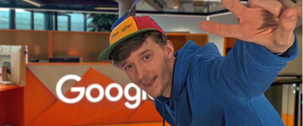 Ben giving the peace sign in front of an orange Google sign while wearing a “Noogler” (new Googler) hat.