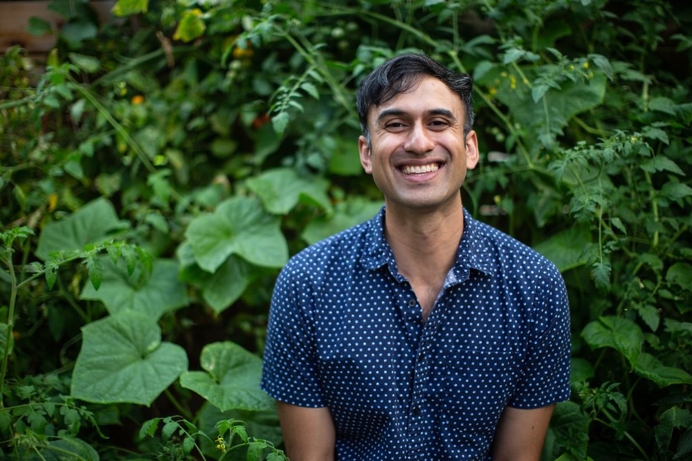 A man standing in front of greenery, smiling at the camera.