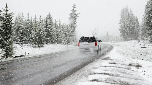 A photo of a car on a road with snow falling