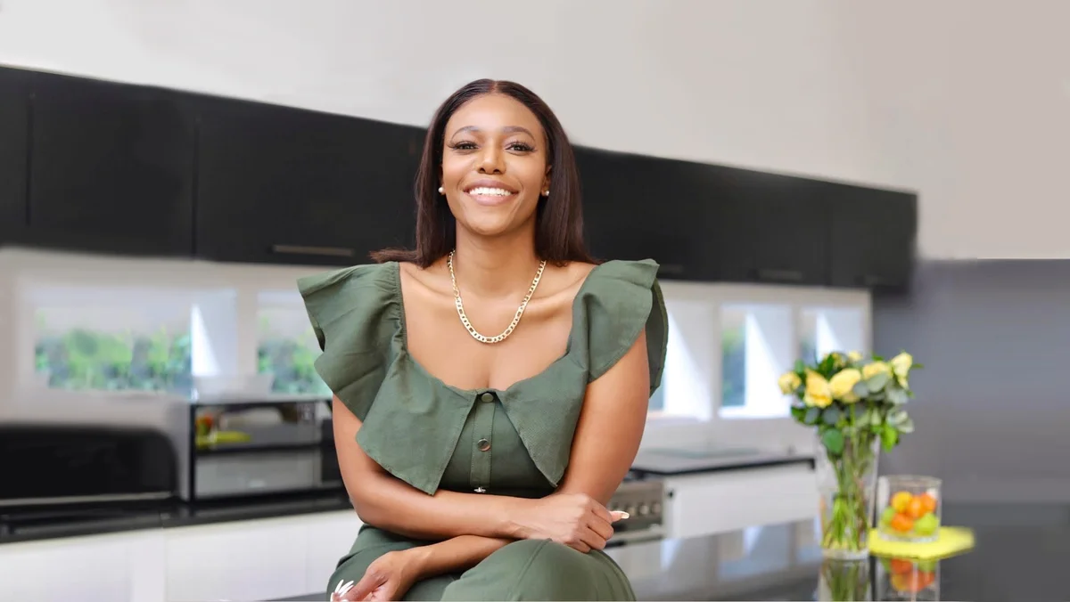 Photograph of a woman sitting in a stylish room, looking into the camera and smiling.