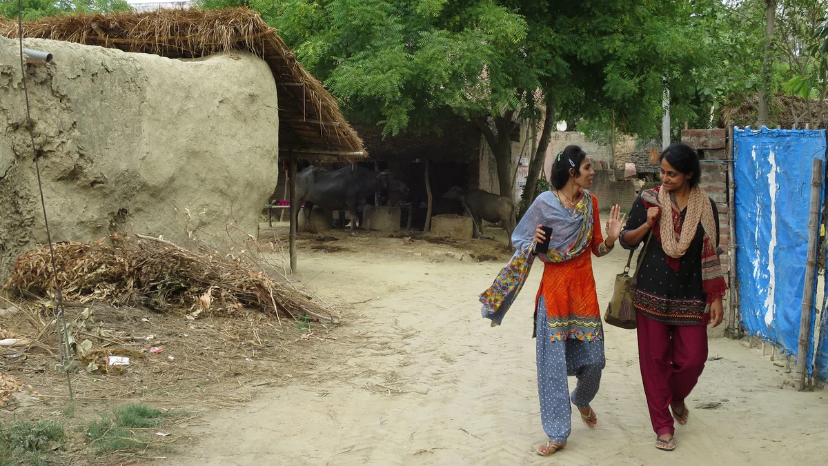 Nithya walking down a road with another person while working in the field.