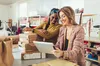 two women looking at a tablet, they're smiling, there are two unopened boxes next to them