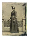 Black-and-white tintype photograph of an African-American woman in 19th century dress standing in front of a fence, taken between 1855-1900