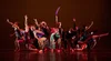 A group of young people dancing on stage, with red lights