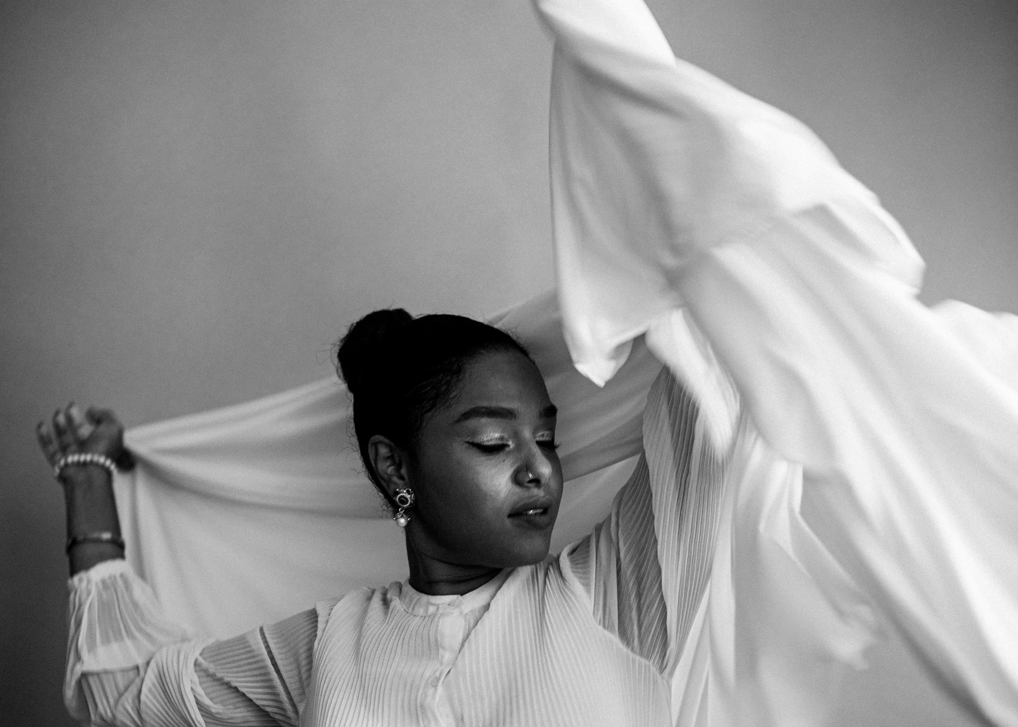 Black and white photo depicting person with white cloth over them and a black background.