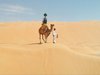 A camel stands atop a sand dune with a Trekker mounted on its back