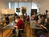 People seated in a classroom, in rows and in front of computers.