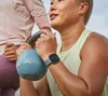 A person in a lime green workout tank lifting a kettlebell while wearing a Fitbit Versa 4.