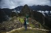 A man stands on a cliff with a camera mounted backpack, overlooking Machu Picchu