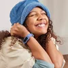 A young girl wearing a denim hat is smiling and wearing a Fitbit Ace 3 with a blue band.