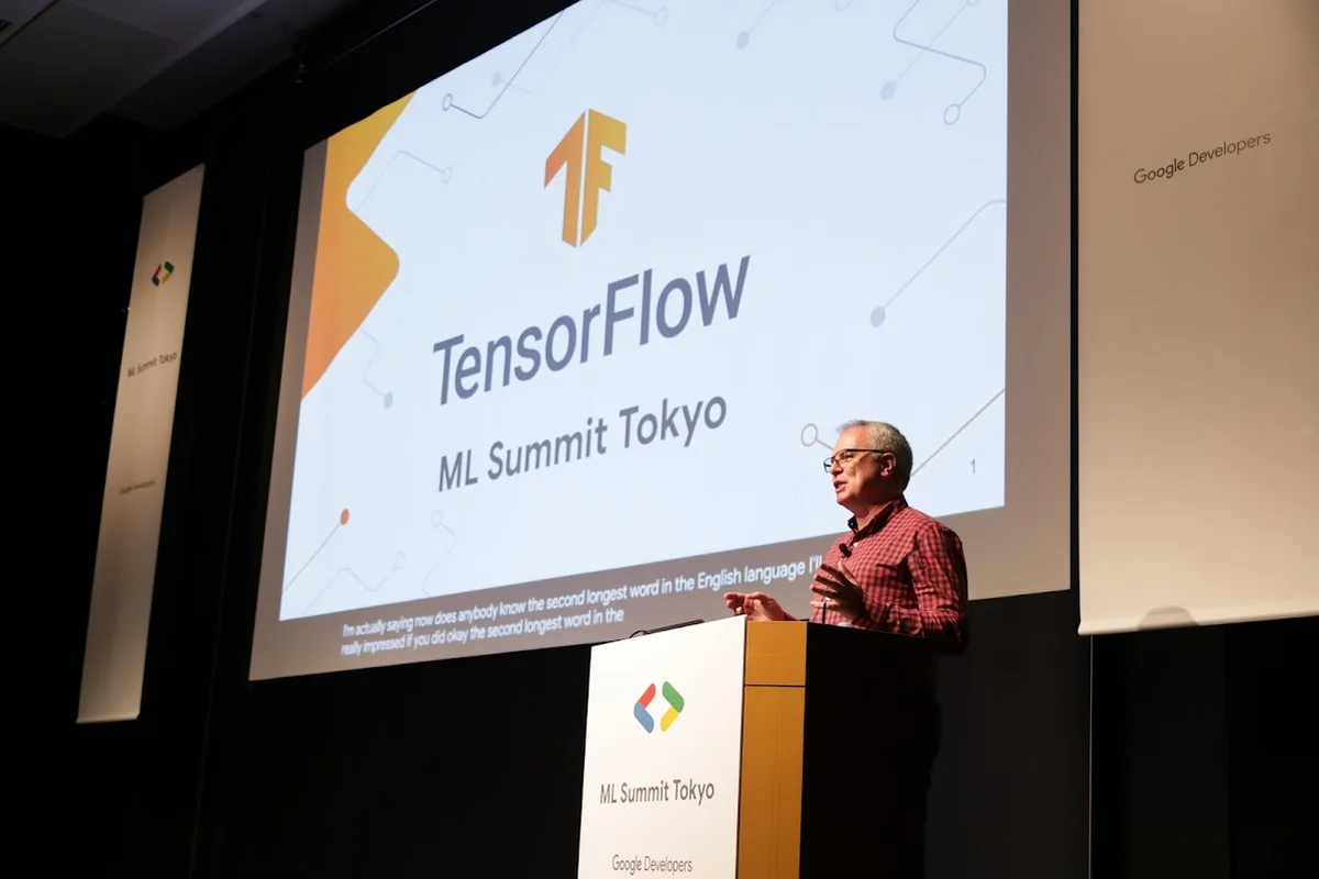 Laurence stands on stage behind a podium. Behind him there’s a project screen with the words “TensorFlow ML Summit Tokyo” projected on it.