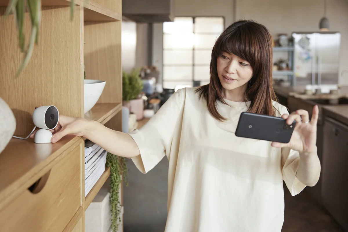 Business owner holds a phone and adjusts a security camera in a kitchen