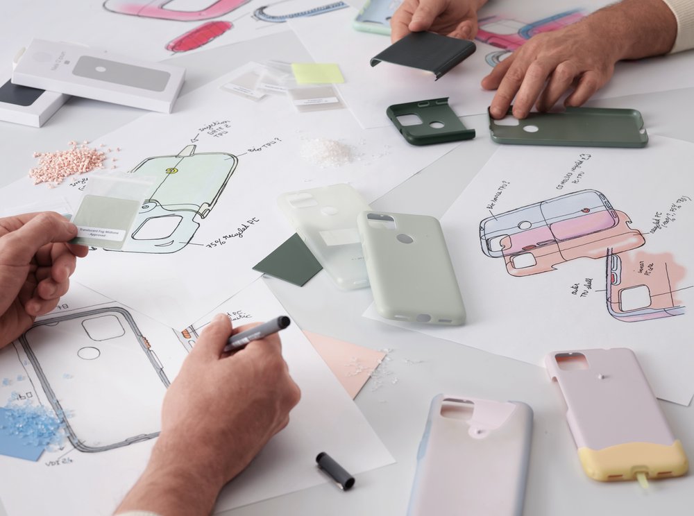 A photo shows the hands of two designers, holding the inner layer of phone case prototypes, working on product sketches and comparing materials.