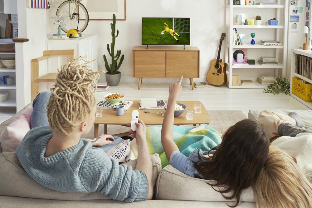 Three friends sit on a couch in the living room watching soccer on the TV with Chromecast with Google TV.