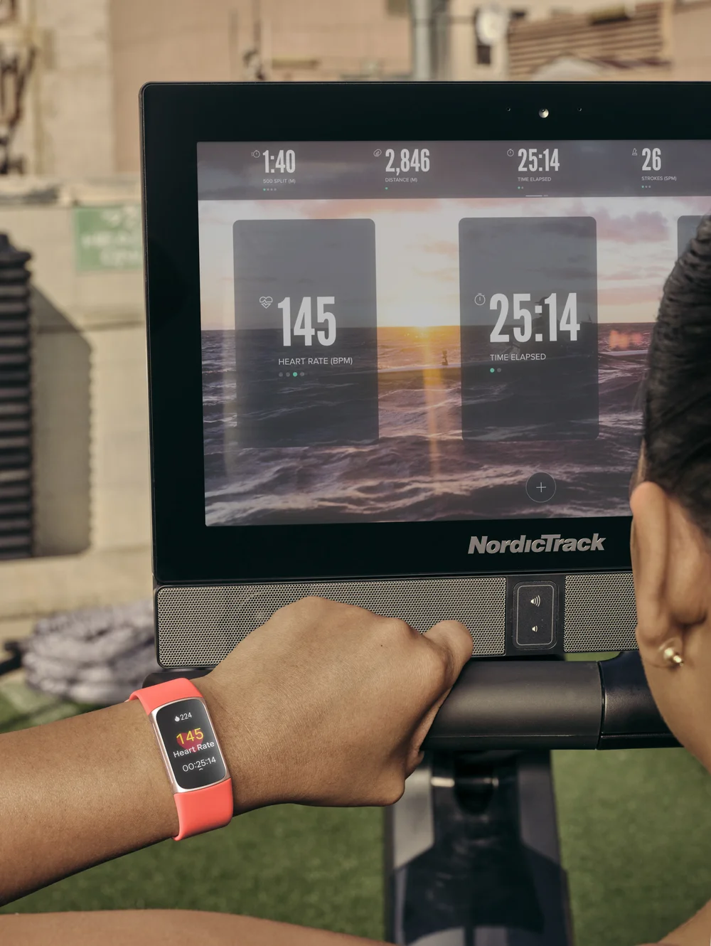 Woman streams her real-time heart rate from Charge 6 in Coral to the screen of a stationary NordicTrack rower.