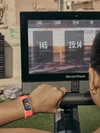 Una mujer transmite su frecuencia cardíaca en tiempo real desde Charge 6 en Coral a la pantalla de un remero estacionario NordicTrack.