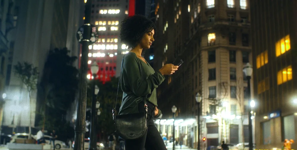 A woman walks on a city street while looking at a mobile phone.