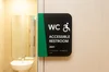 Sign in front of a bathroom that reads "accessible restroom" with braille underneath