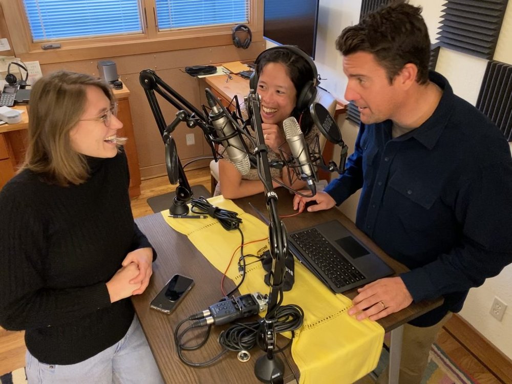 This is a photo of three individuals around a table and microphones.