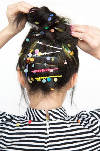 Photo of the back of a woman's head with hair clips that read 'Friday,' 'Whatever,' and 'Party.'