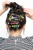 Photo of the back of a woman’s head with hair clips that read “Friday,” “Whatever,” and “Party.”