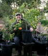 Kevin Espiritu sits on a bench. Between his legs is a small potted tree with one orange.