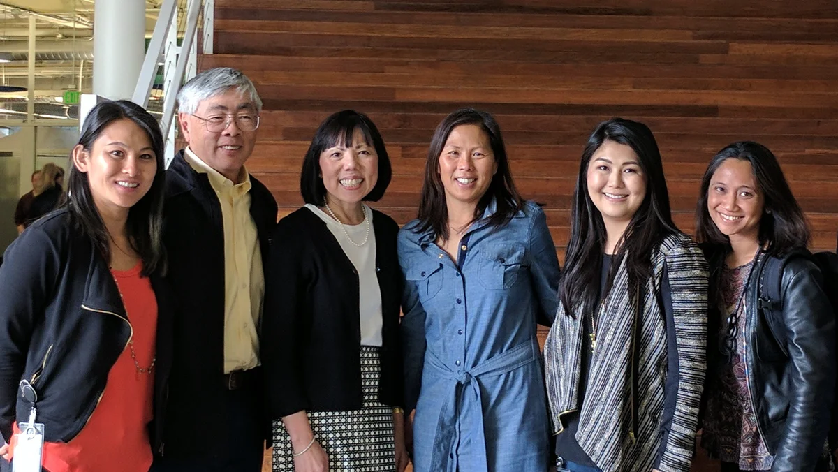 A group of six, Lisa Lee is in the middle in a blue dress. The group is smiling in front of a solid wood backdrop during a recent Asian Googler Network Employee Resource Group event
