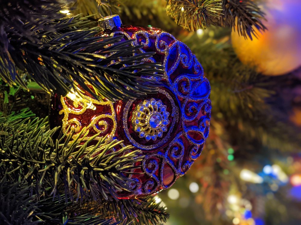 Image showing a macro shot of an ornament hanging in a tree. The lights are low and there is decorative lighting, but the ornament remains in focus while the background is blurry.