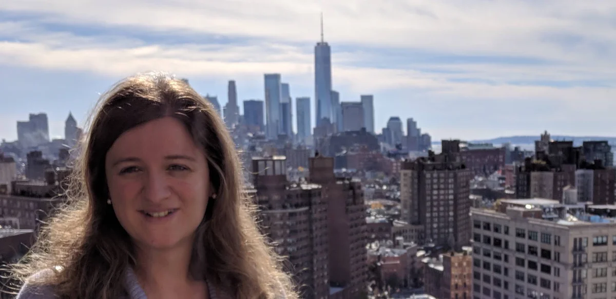 Image of a woman looking into the camera and smiling with a city in the background behind her.