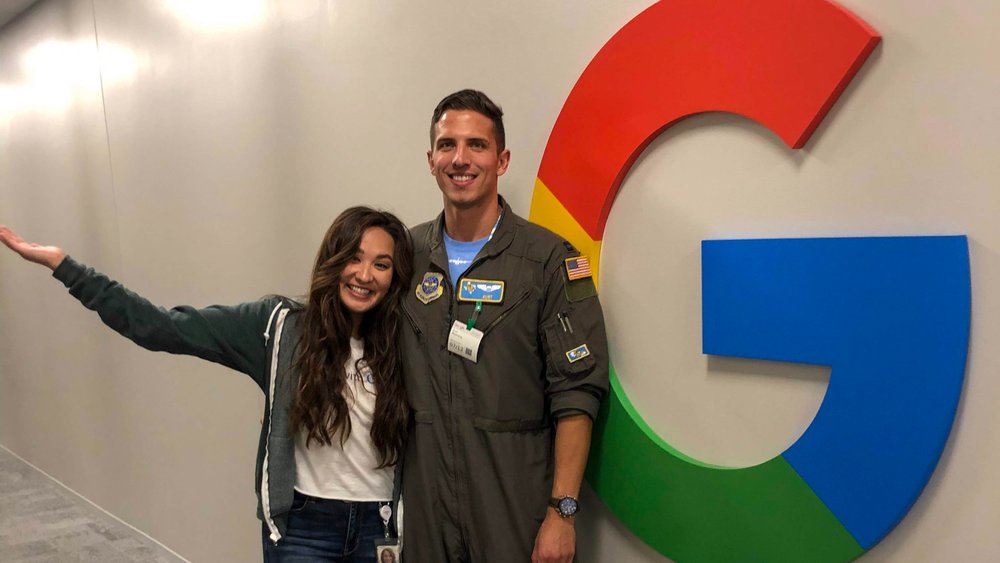 Bry and her husband, wearing a military uniform, stand in front of a Google logo