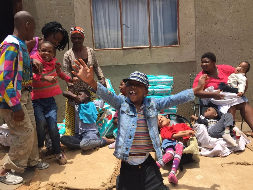 Young boy with arms outstretched looking happy with piles of nappies in the background