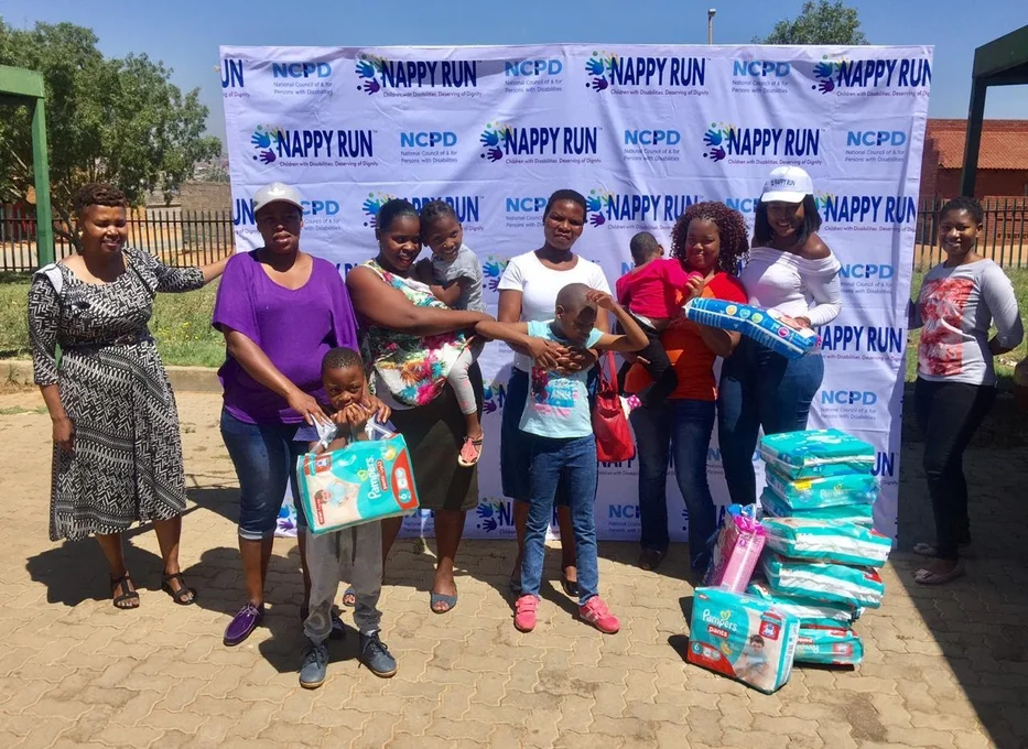 A crowd of people next to packs of nappies and in front of a promotional wall with Nappy Run branding