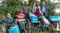 Three children in wheelchairs with accompanying adults and a stack of nappies besides them