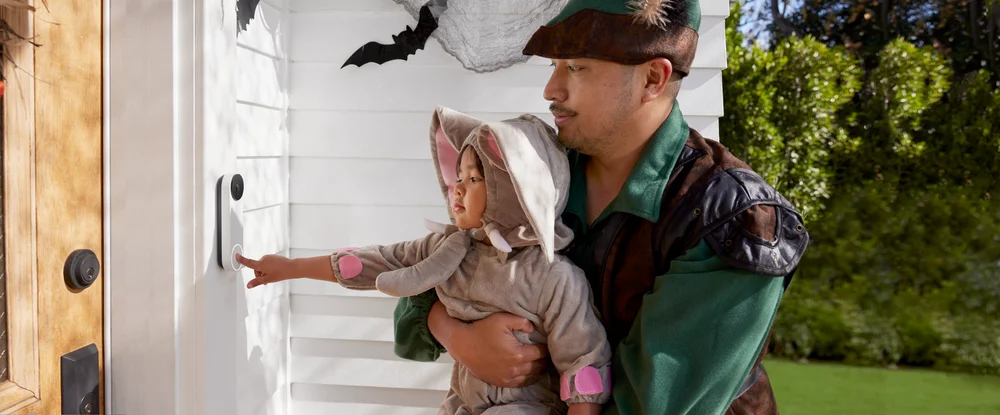 An adult and child wearing costumes ringing a Nest Doorbell (battery) at someone’s door.